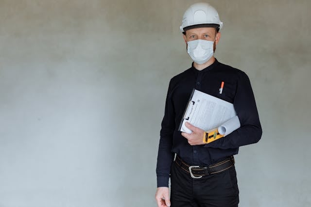 a contractor in a mask and hard hat holding a clipboard
