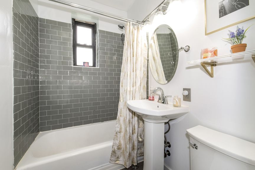 Bathroom with grey tile, pedestal sink, and circular mirror