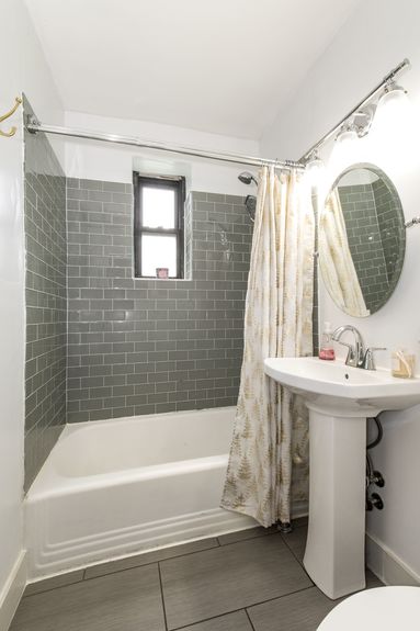 Bathroom with grey tile, pedestal sink, and circular mirror