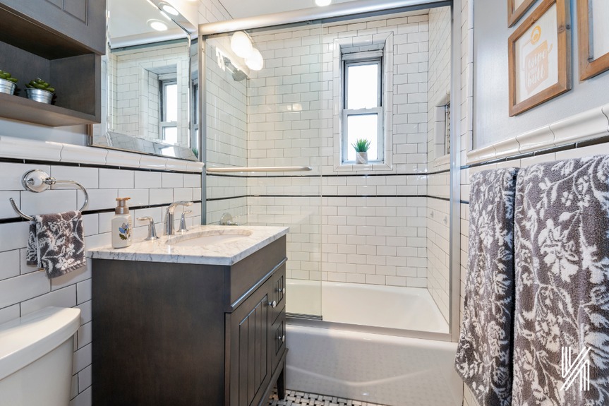 Full bathroom with a glass-enclosed tub with a niche, floor-to-ceiling subway tiles, carrera marble basketweave floors, marble vanity top, and a mirrored medicine cabinet
