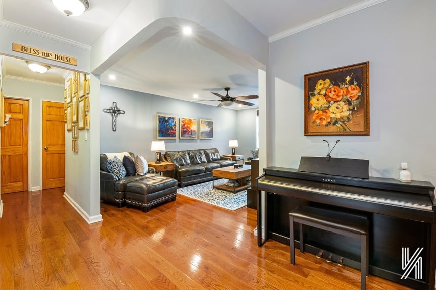 Living room view from the kitchen with soundproofed hardwood floors, couches, a piano, and beautiful paintings