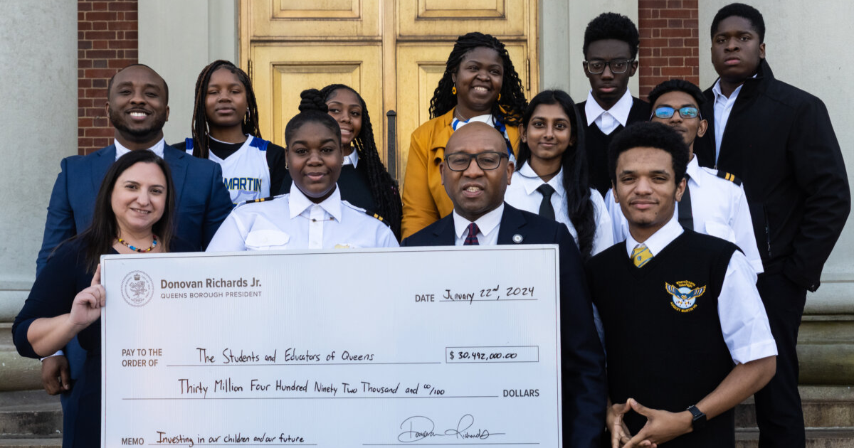 Queens Borough President Donovan Richards, AMHS principal Allison Tiberio, and students are pictured holding a check bearing the memo "investing in our children and our future."