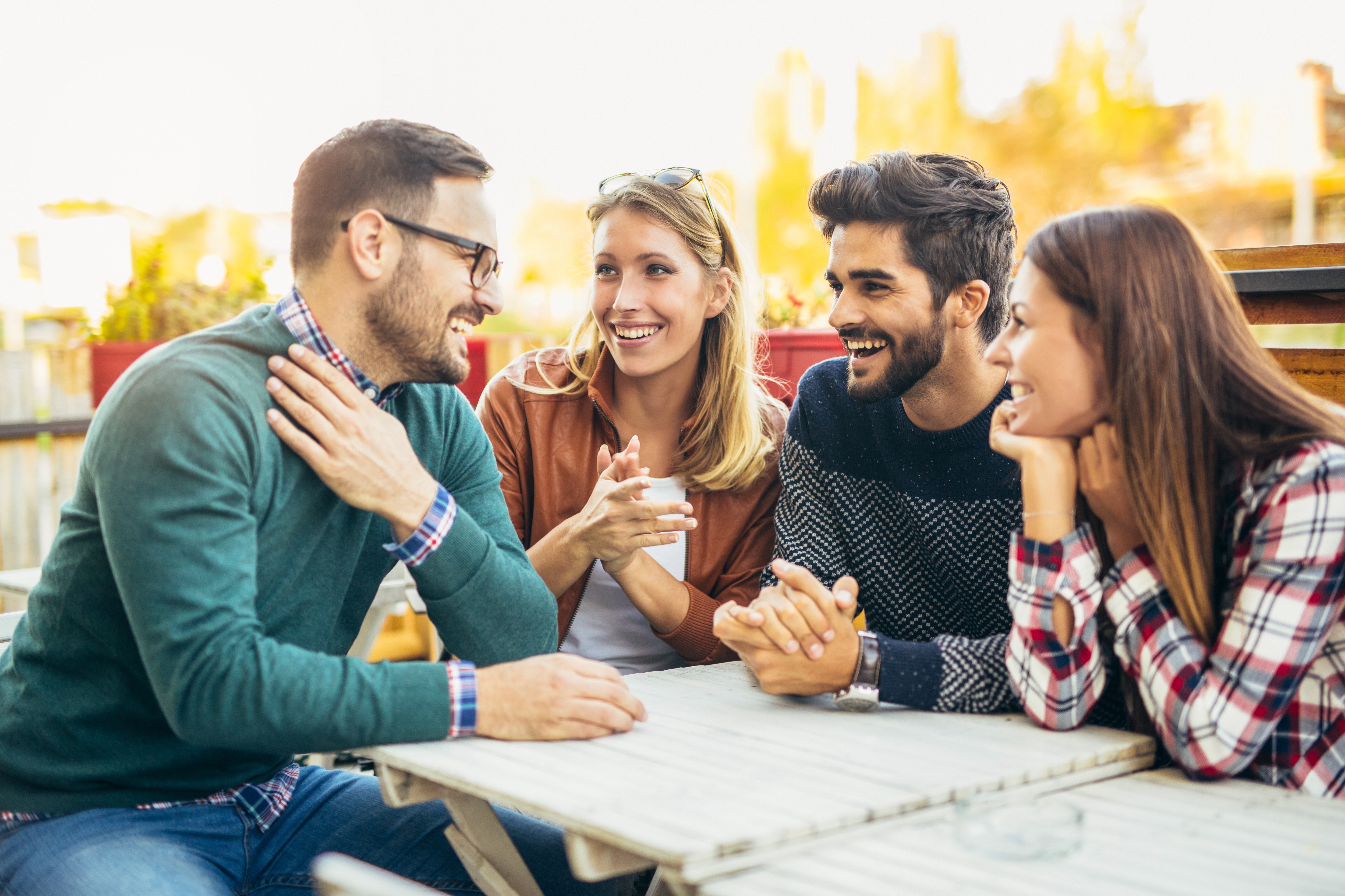 Group of four friends having fun a coffee together. Two women and two men at cafe talking laughing and enjoying their time