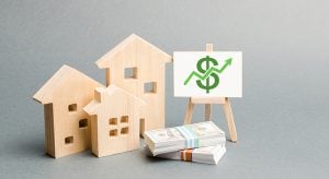 Wooden figures of houses and a poster with money. The concept of real estate value growth. Increase liquidity and attractiveness of assets. Raising the rent or cost of buying a home.