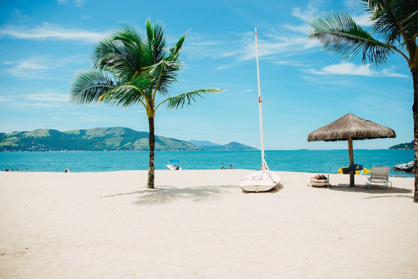 Palm trees and white sand beach with a sailboat