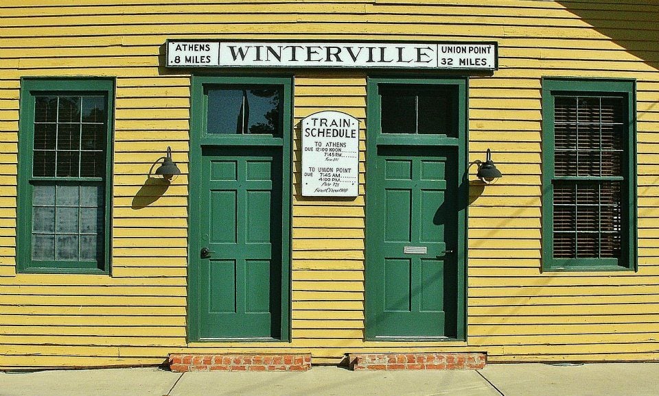 Yellow clapboard Winterville train depot with green doors and a vintage station sign