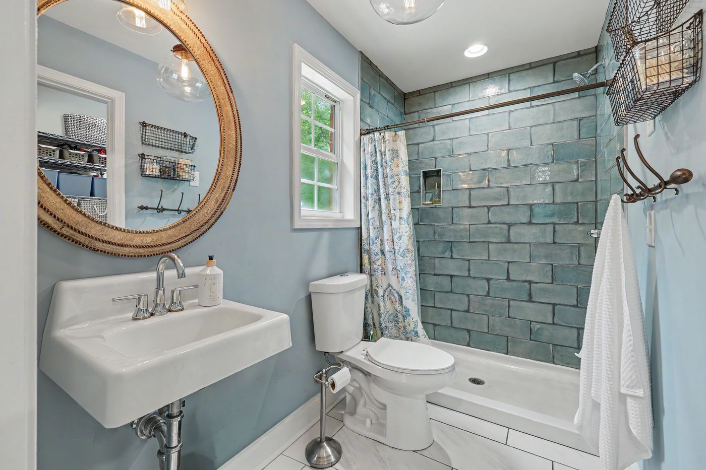 Bath with blue glass subway tile and round rattan mirror