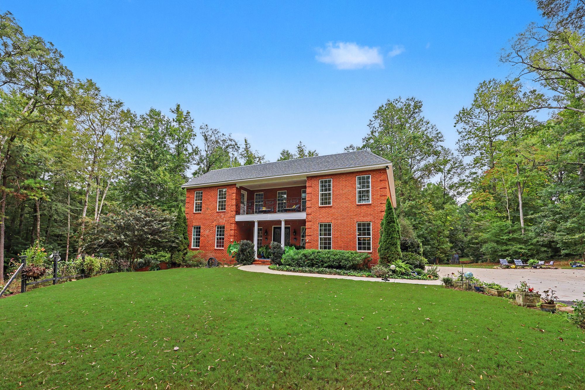Two-story brick home with upper balcony set on a wide lawn