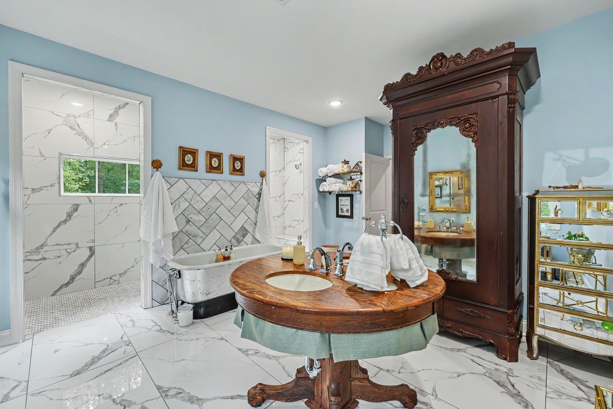 Primary bath with antique pedestal vanity and carved armoire