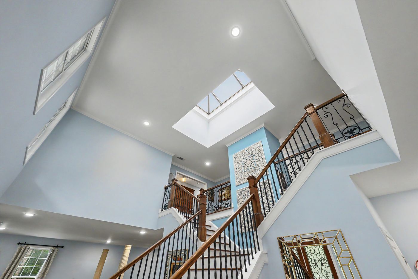 Sweeping staircase with wrought-iron balusters rising to a skylight