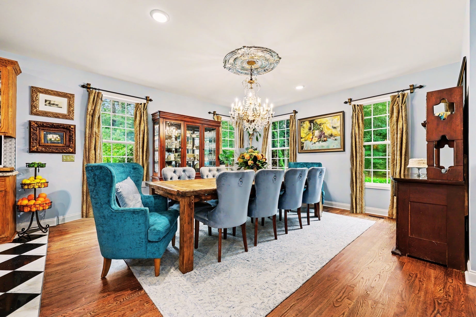 Light-filled dining room with a crystal chandelier, teal wingback chairs and gallery walls