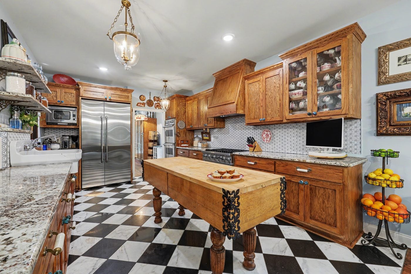 Kitchen with oak cabinetry, antique butcher-block island and black-and-white marble floor