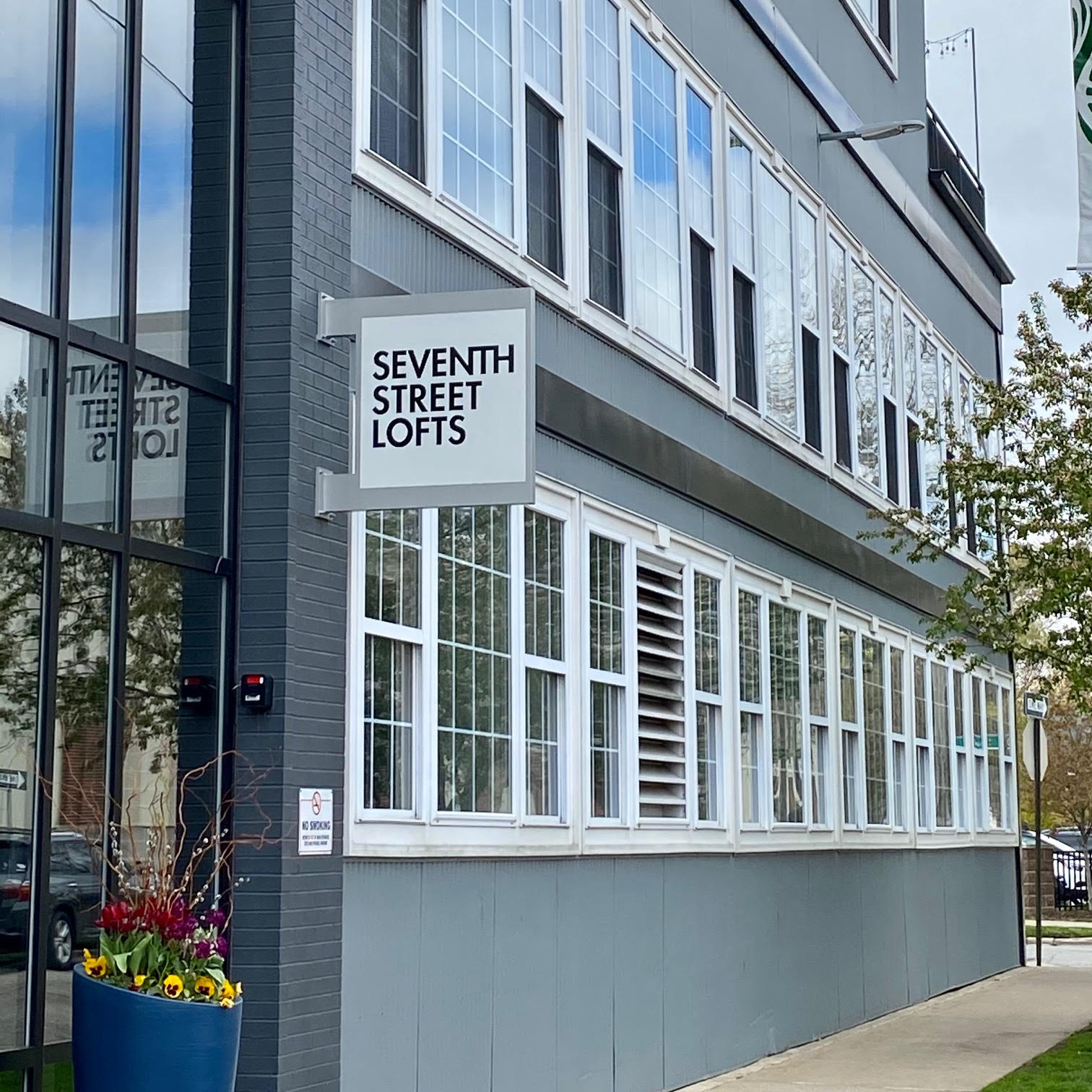 Exterior of Seventh Street Lofts in Grand Rapids, showing a “Seventh Street Lofts” sign on a gray brick facade with rows of white‑framed windows.
