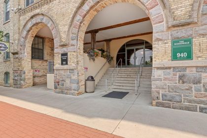Close‑up of Boardwalk Condos entrance featuring three limestone-and‑brick arches, stone steps leading to glass doors, and a green “940 Monroe” sign on the right pillar.