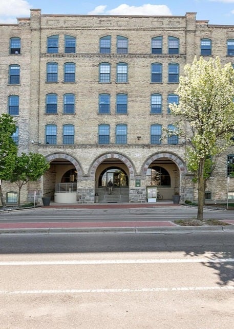 Front view of Boardwalk Condos in Grand Rapids, a five‑story blonde‑brick building with three large stone archways framing the main entrance.
