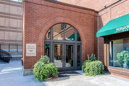 Close view of the arched glass entrance marked “252 Pearl St” with brick surround, potted greenery, and a Forslund Condominium plaque.