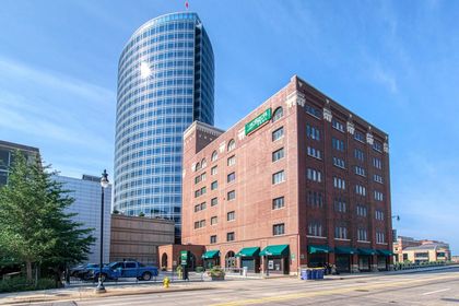 Street‑level view of Forslund Condominium’s red‑brick façade with green awnings, modern glass skyscraper rising behind.