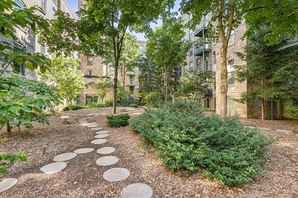 Lush courtyard planted with mature trees and shrubs, featuring a curved stepping‑stone walkway over mulch between the condo building wings.