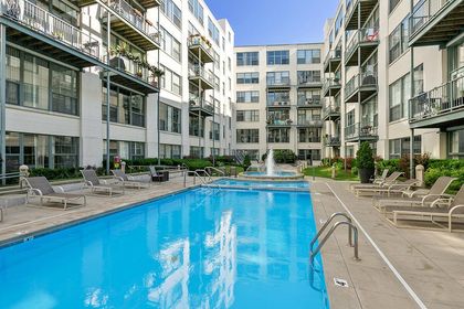 Long rectangular outdoor pool bordered by tan lounge chairs, with condo balconies above and a circular fountain at the far end.