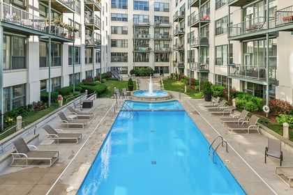High angle view of the courtyard pool and surrounding lounge area, showing the fountain, pool ladder, and rows of condo balconies looking inward.