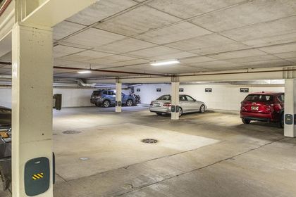 Interior of a well‑lit, concrete underground parking garage with marked resident spots and several parked vehicles.