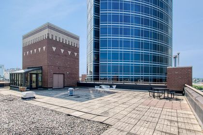 Open rooftop deck with paver tiles, scattered café tables, and the blue‑glass River House tower looming next door.