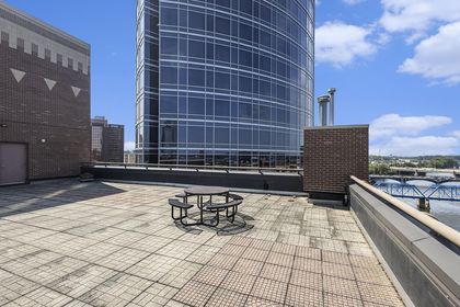 Rooftop terrace showing a round metal picnic table, brick chimney, River House tower, and Blue Bridge / Grand River in the distance.