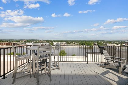 Close‑up of a high round table with four chairs on the Boardwalk rooftop deck, overlooking the Grand River and cityscape beyond.