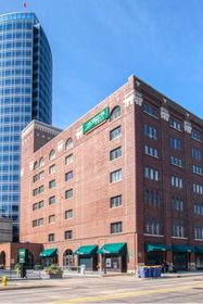 Tall street view of Forslund’s brick façade and green awnings with the glass River House skyscraper rising behind.