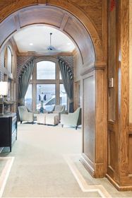 Interior perspective through a wood‑trimmed arch toward a seating nook with arched brick windows and armchairs.