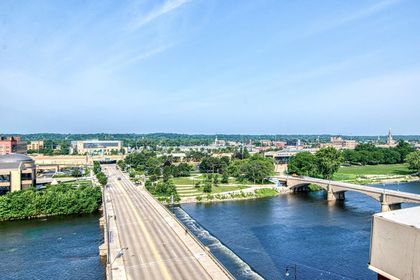 Elevated view of Grand River, Pearl Street Bridge, riverside park, and downtown skyline in the distance.