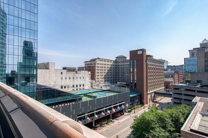 Elevated view toward eastern downtown with glass high‑rise, hotel towers, rooftop sports court, and city street below.