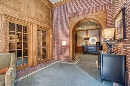 Interior shot of a wood‑trimmed brick archway leading from the lobby to interior hallways, with carpeted floors and accent furniture.