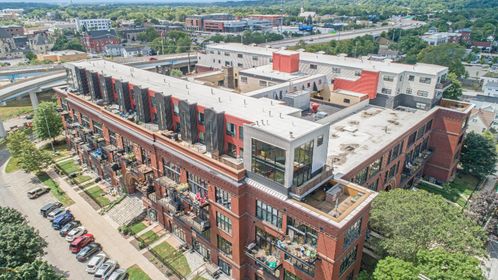 Diagonal drone shot of the building’s brick façade and rooftop townhomes with red and charcoal panels.