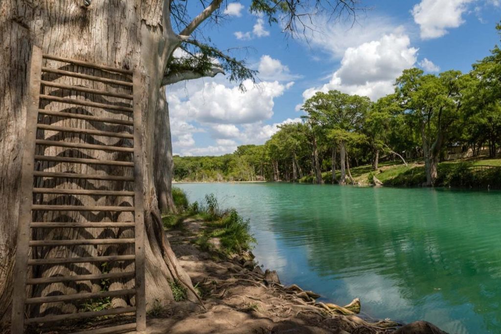 View of the Blanco River from 7A Ranch & Resort, with trees lining the riverbank and clear water.