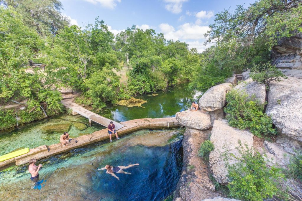 A clear, natural spring opening at Jacob’s Well in Texas, surrounded by limestone and greenery.