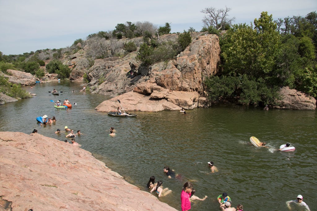 Friends and families enjoying swimming, paddling, and relaxing together in clear waters of Inks Lake on a sunny Texas day.