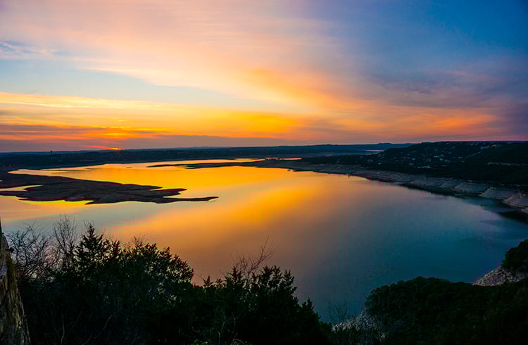 Lake Travis sunset over the Hill Country, highlighting the choice between wellness-focused living and luxury waterfront lifestyles.