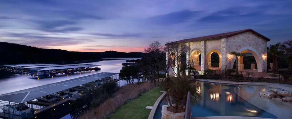 Luxury lakefront home overlooking Lake Travis with marina views, sunset sky, and resort-style outdoor living spaces