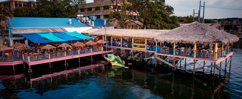 Hula Hut restaurant on Lake Austin with colorful tiki-style waterfront deck, open-air seating, and dockside dining over the water