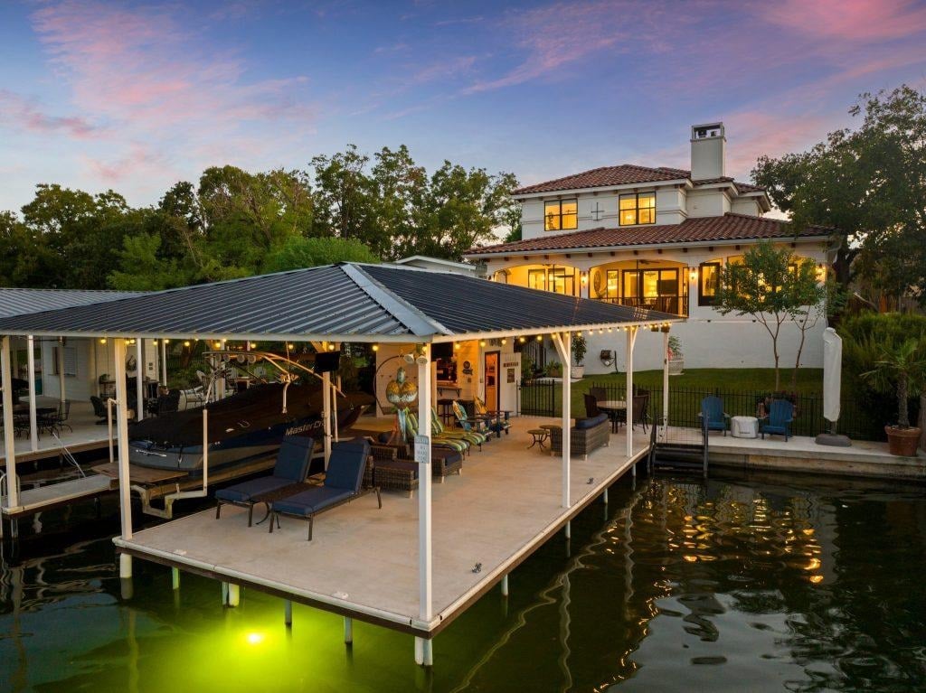 Lake LBJ waterfront home featuring private boat dock, covered outdoor seating area, boat lift, and lakeside entertaining space at sunset